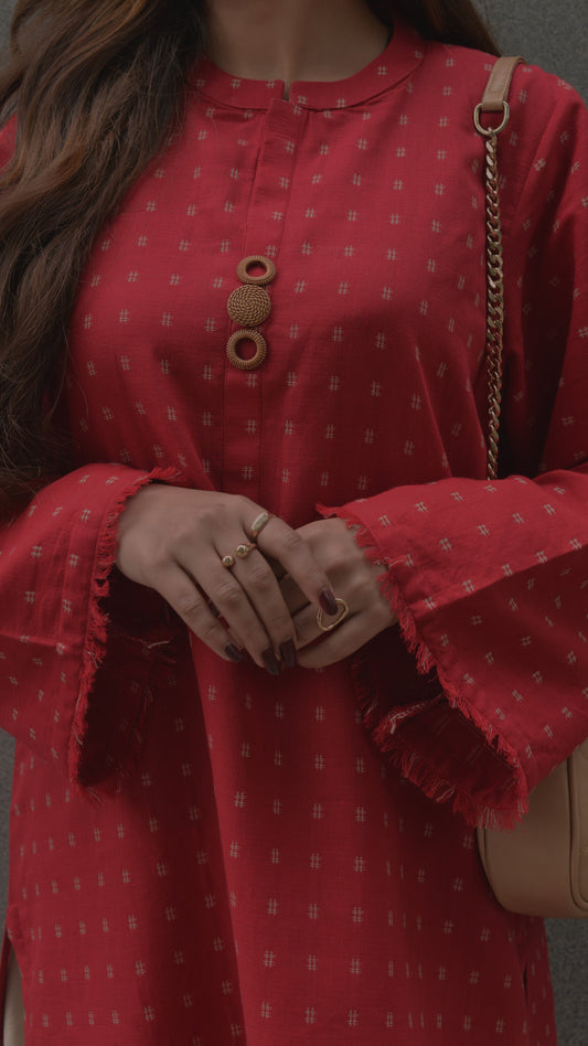 Red patterned dress with bell sleeves worn by a person, holding a beige handbag.